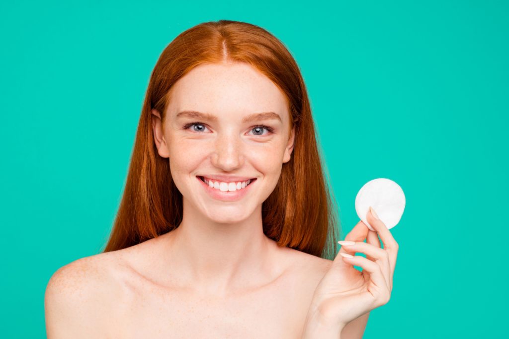 Close-up portrait of nice nude positive cheerful red-haired girl with shiny pure clean fresh smooth flawless skin, holding, showing cotton pad, spa, therapy, treatment, isolated over green turquoise background Close-up portrait of nice nude positive cheerful red-haired girl with shiny pure clean fresh smooth flawless skin, holding, showing cotton pad, spa, therapy, treatment, isolated over green turquoise background