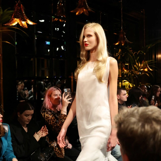 Modelka ubrana w sukienkę przechadza się po wybiegu.