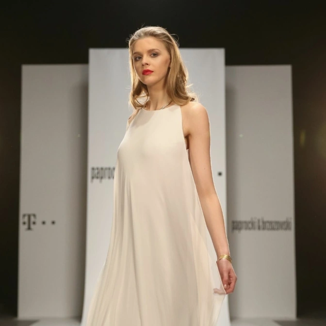 Modelka pozuje na wybiegu w białej sukni.