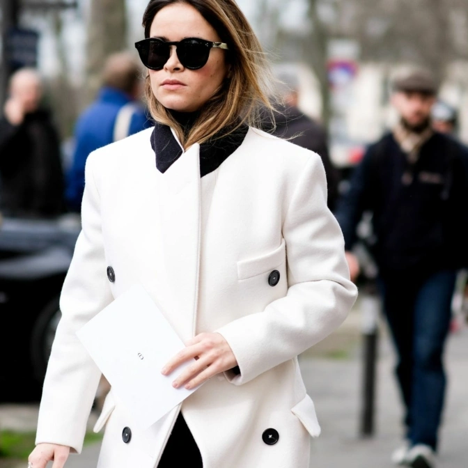 Kobieta ubrana w biały płaszcz idzie ulicą.